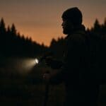 Prepper holding tactical flashlight, watching for threats at dusk.